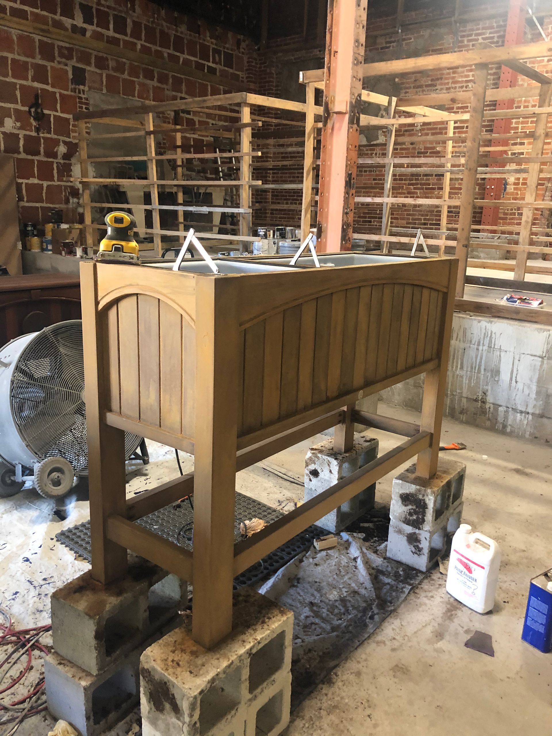 Wooden furniture piece being worked on in a workshop, resting on cinder blocks.