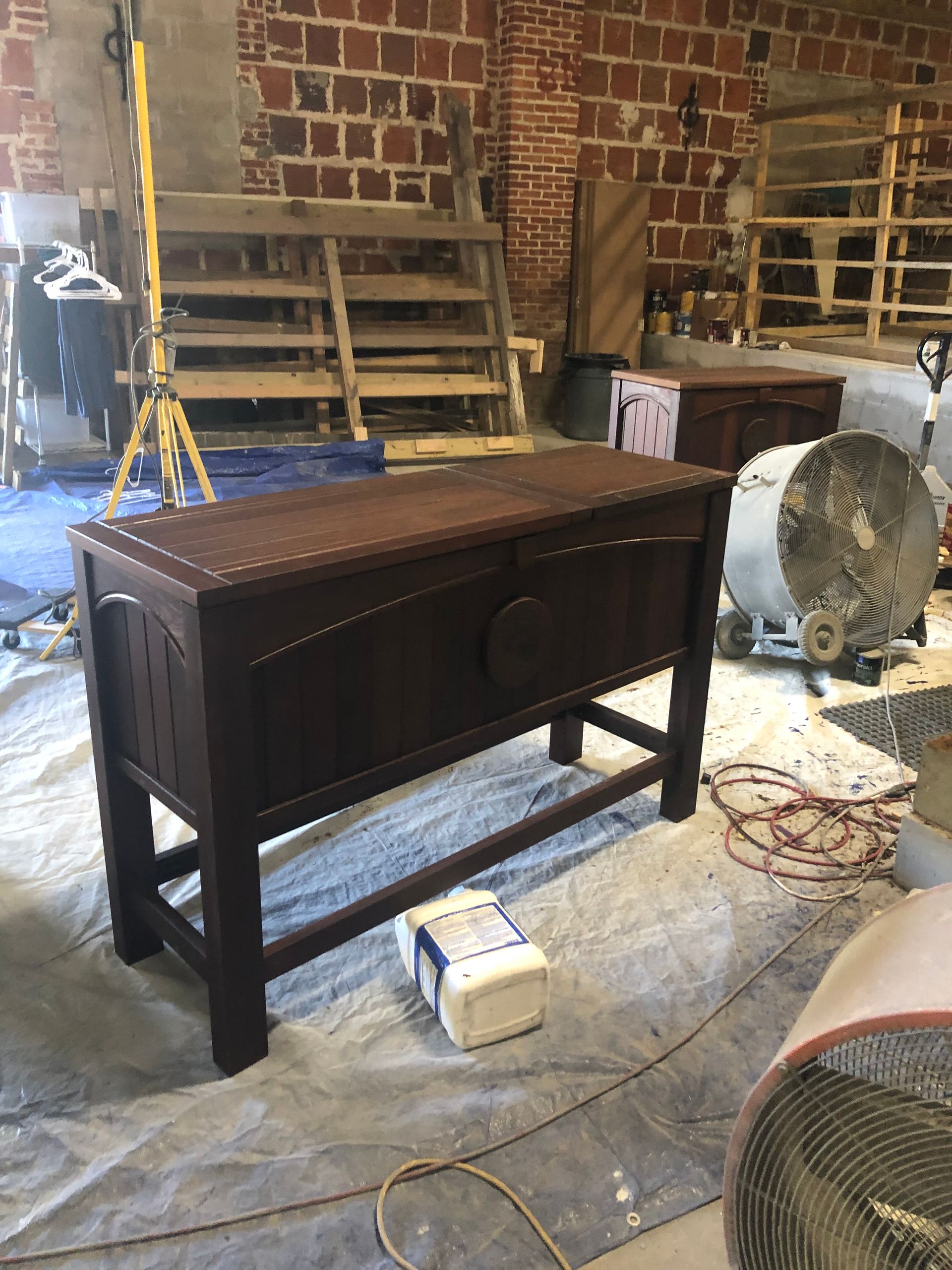 Dark stained wooden chest on a tarp in front of a brick wall, inside of a workshop.