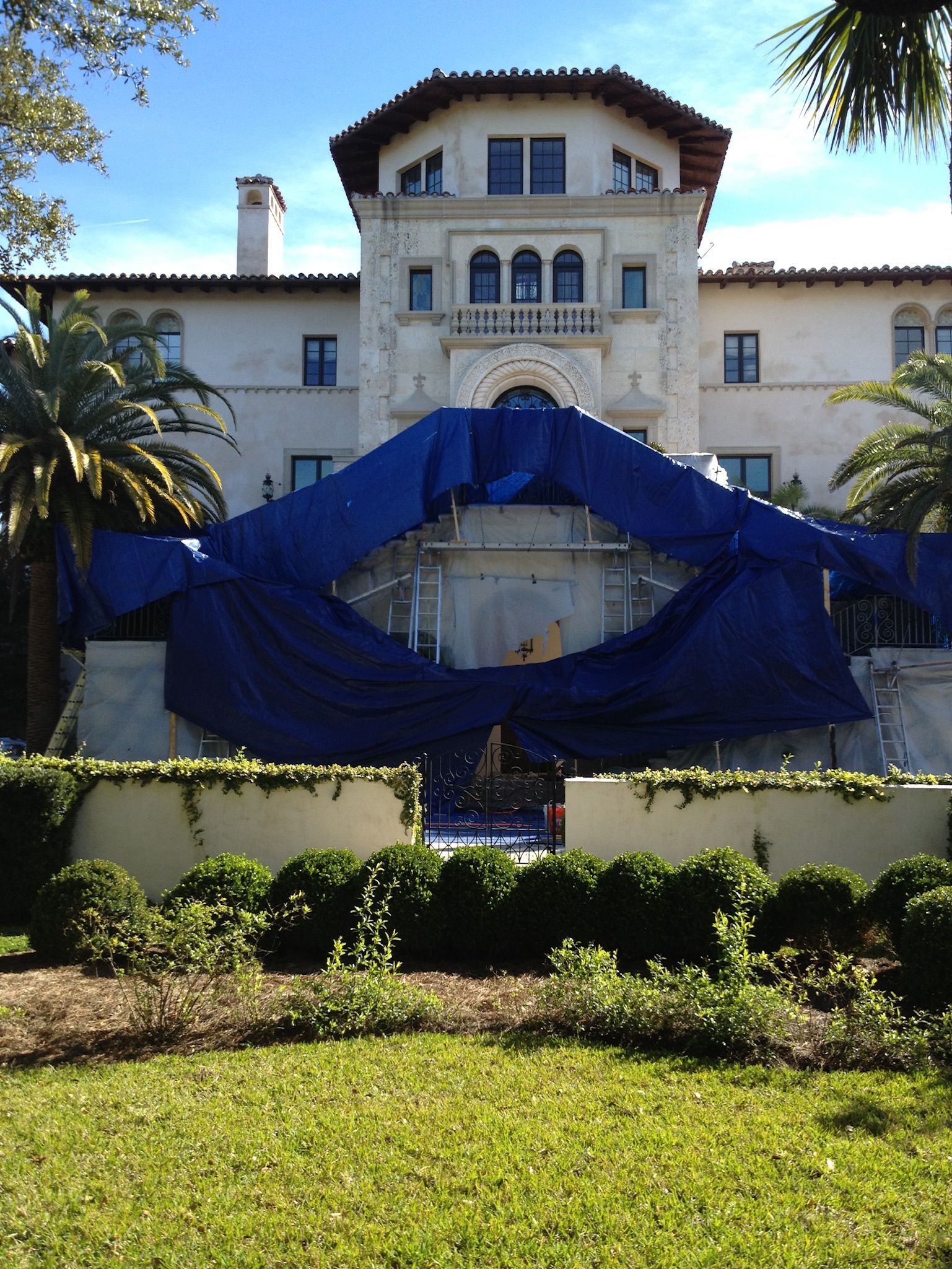 A large white building with blue tarps covering a structure, set against a blue sky.