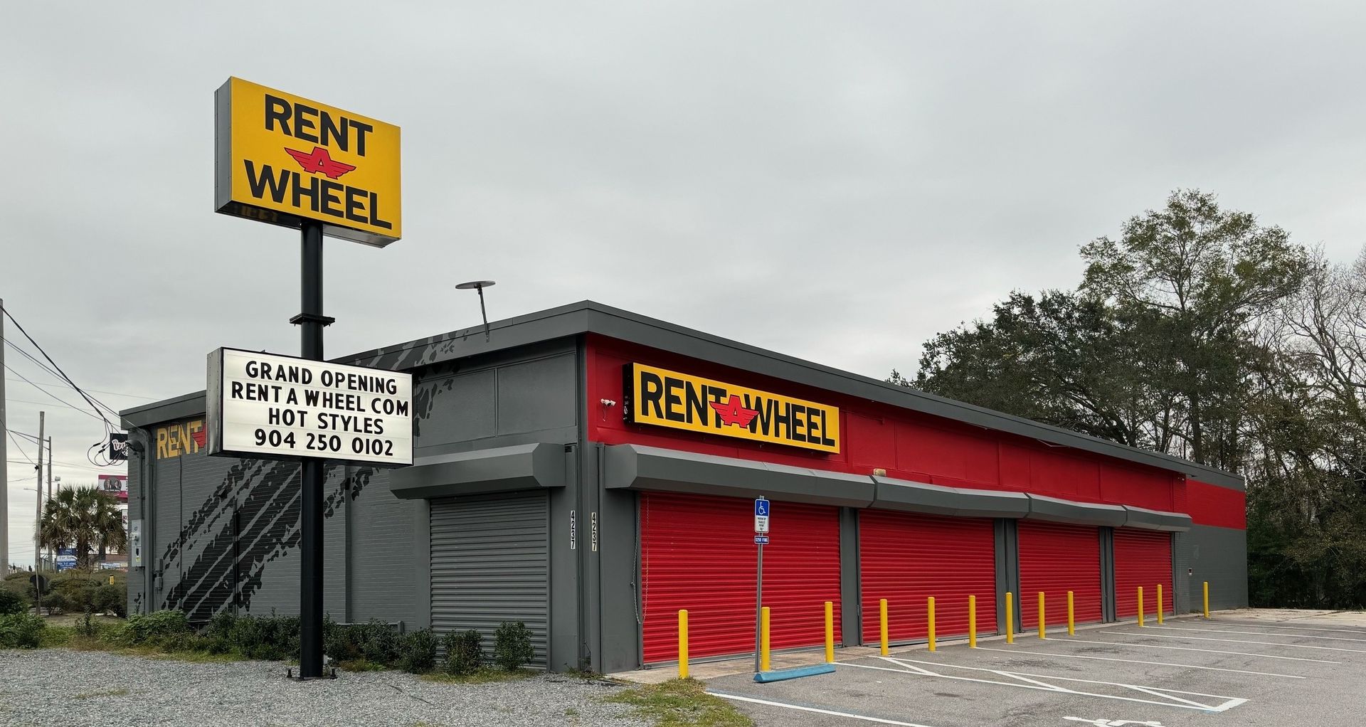 Rent-A-Wheel building with red and gray facade. Sign with business name in red and yellow. Black rollup doors.