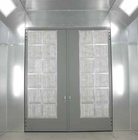 Closed gray double doors inside a bright, enclosed paint booth with lighting fixtures.