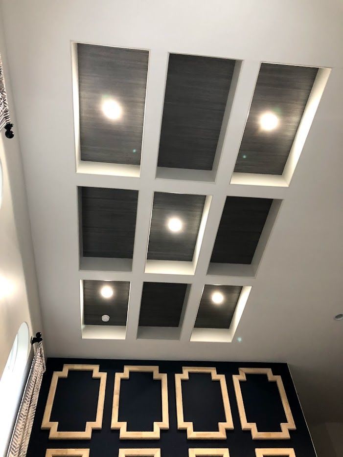 Rectangular ceiling with recessed lighting, dark gray panels, and decorative wall with gold trim.