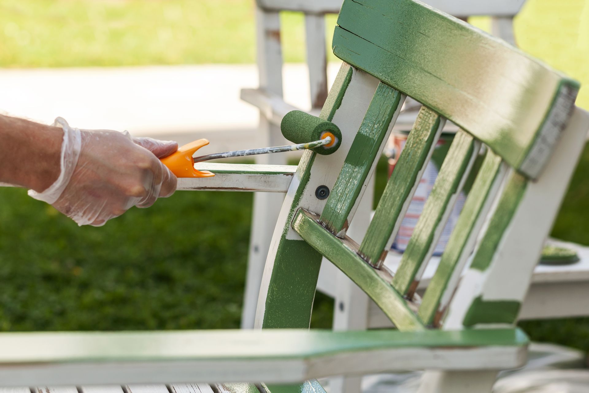 A person is painting a green chair with a roller.