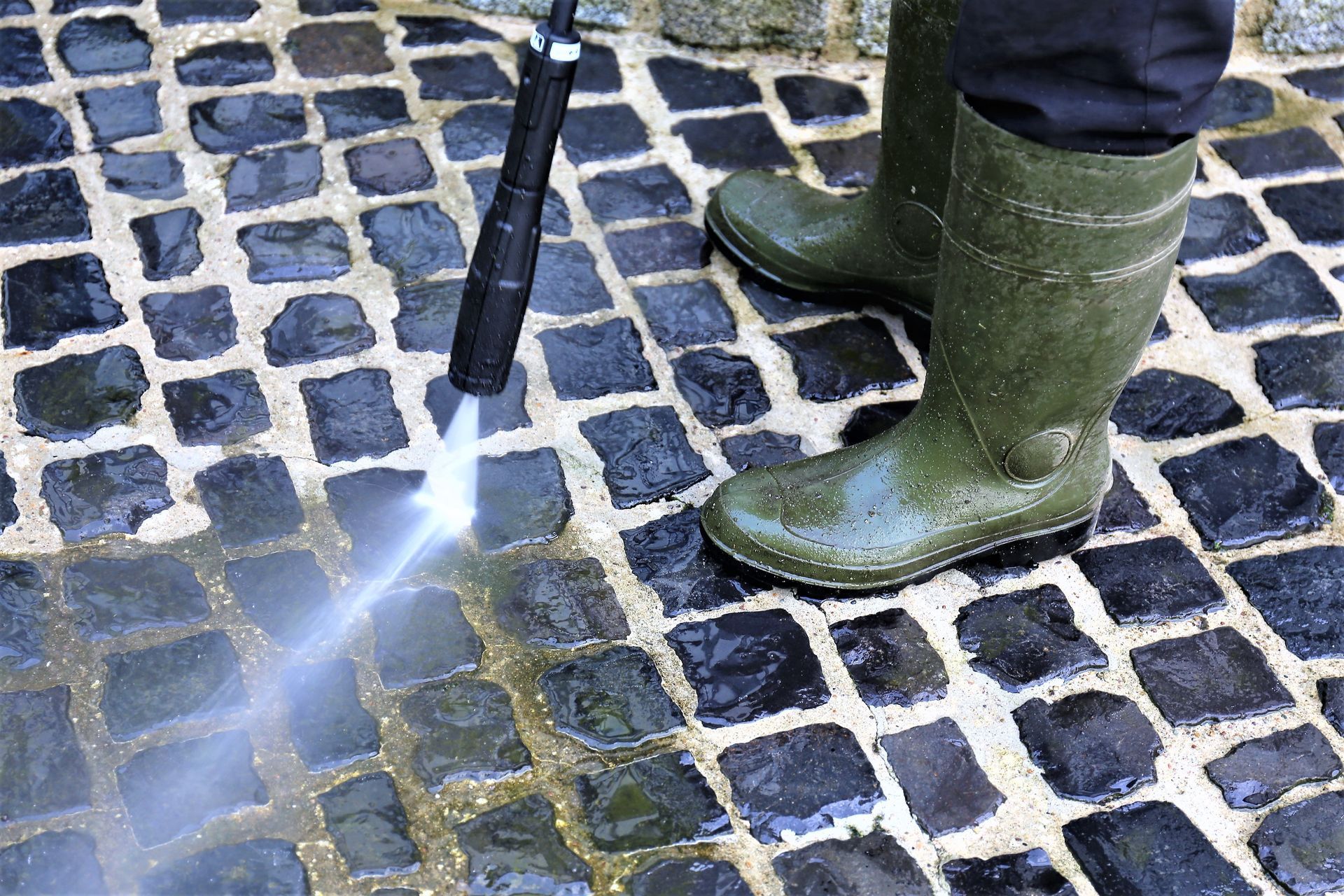 A person is using a high pressure washer to clean a cobblestone floor.