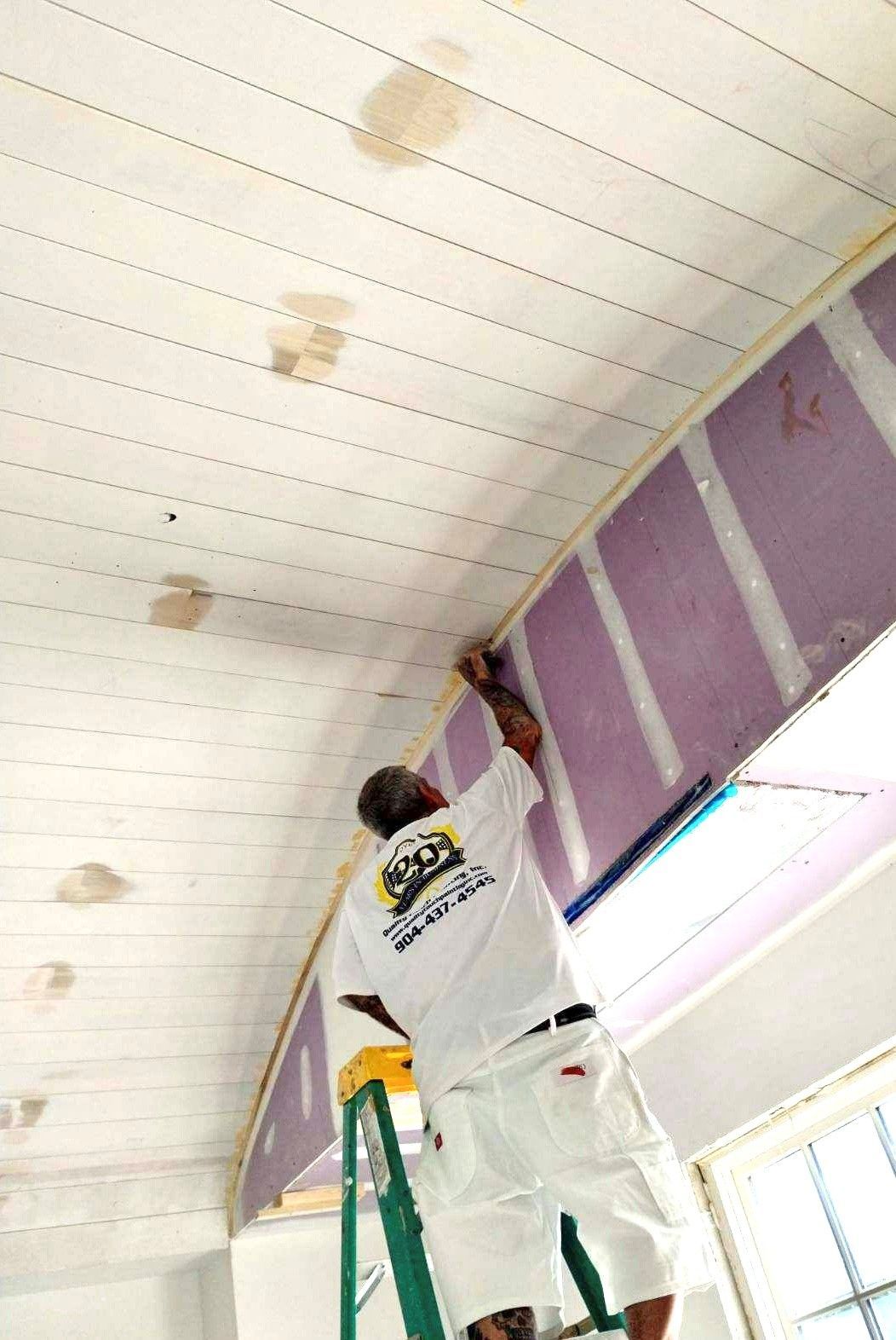 Man on ladder taping ceiling; purple insulation visible. White walls, light colors.