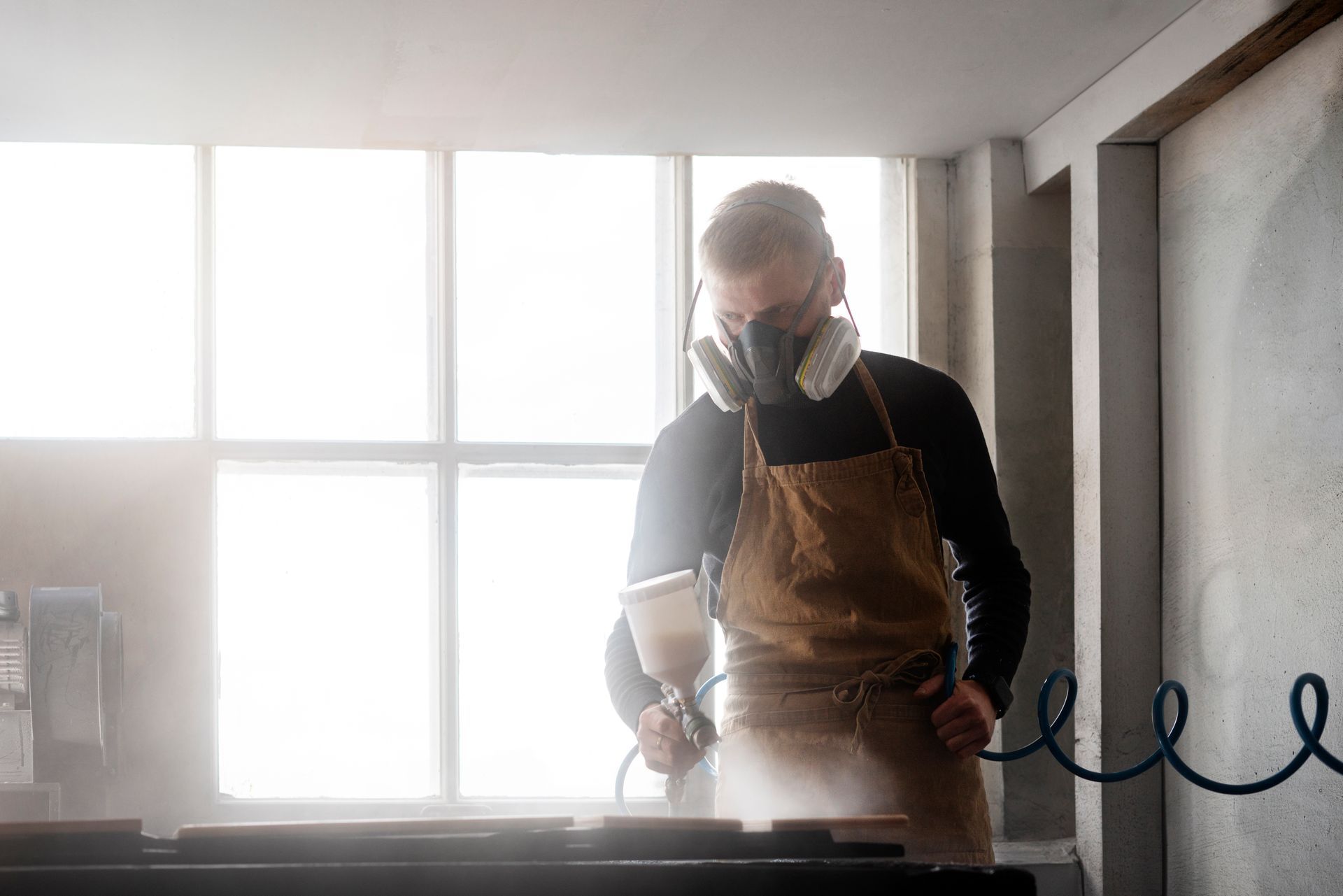 A man wearing a gas mask is painting a piece of wood.