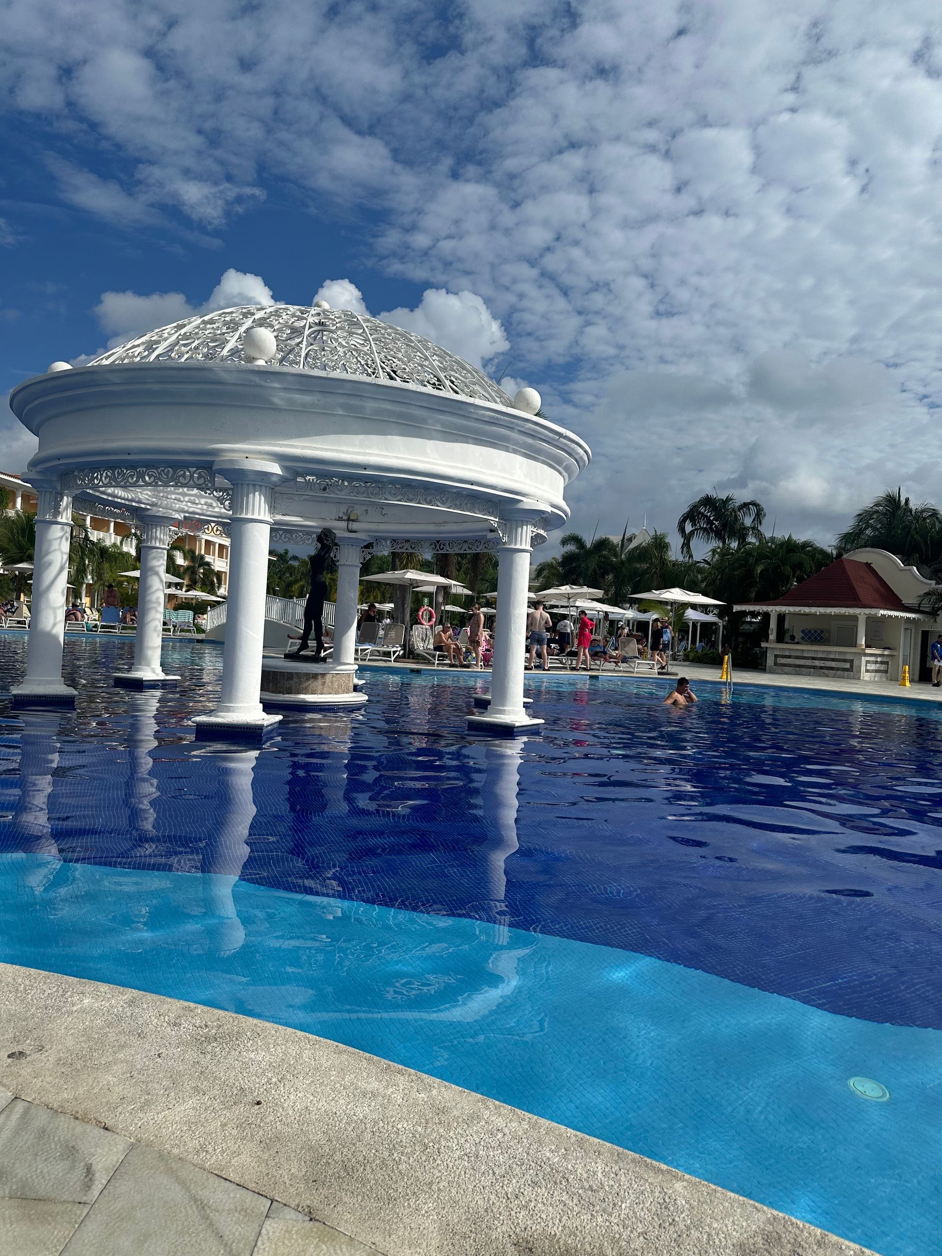 Swimming pool with white gazebo, blue water, and partly cloudy sky.