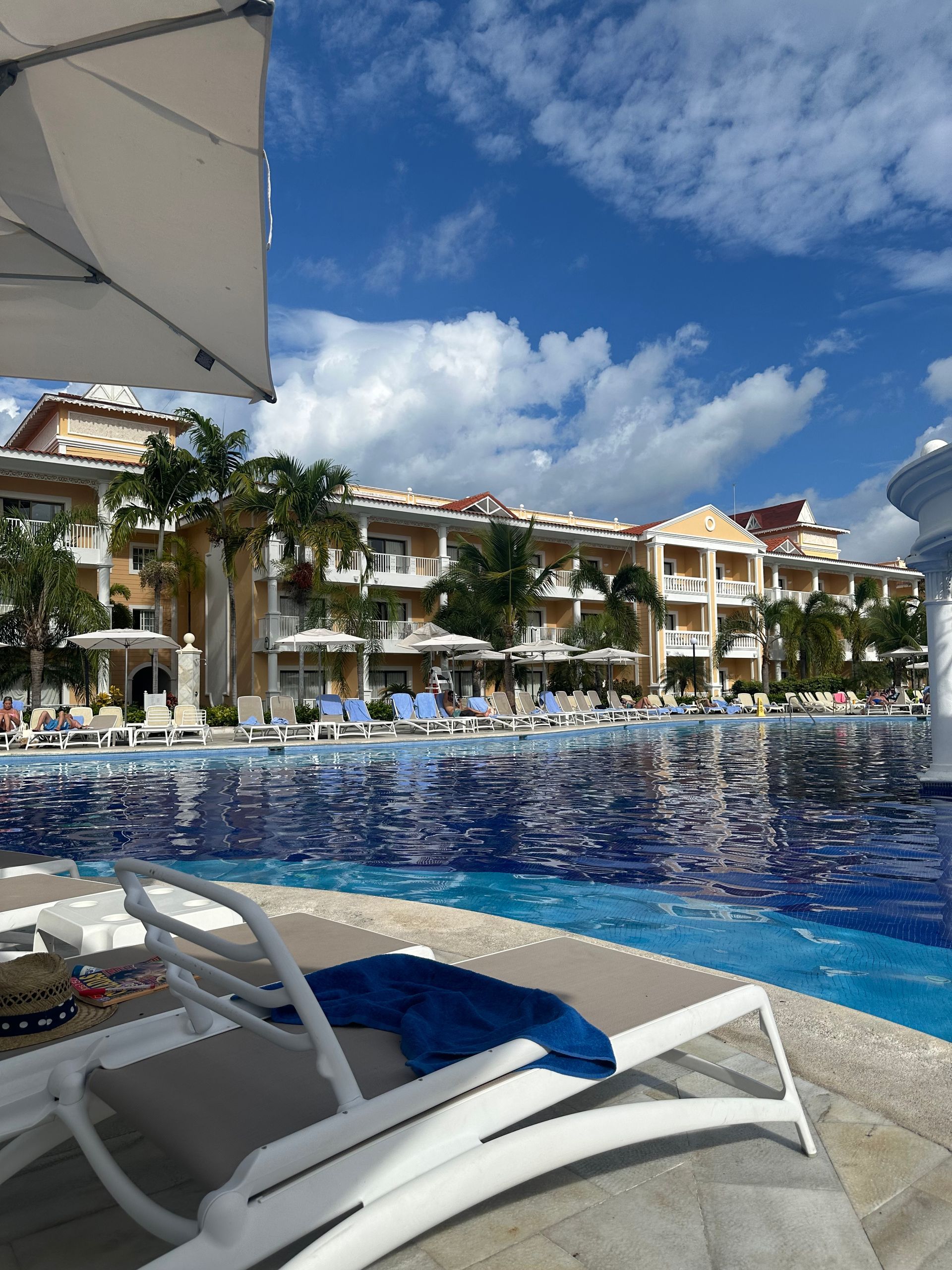 Poolside view of a resort with buildings, blue sky, and white umbrellas.