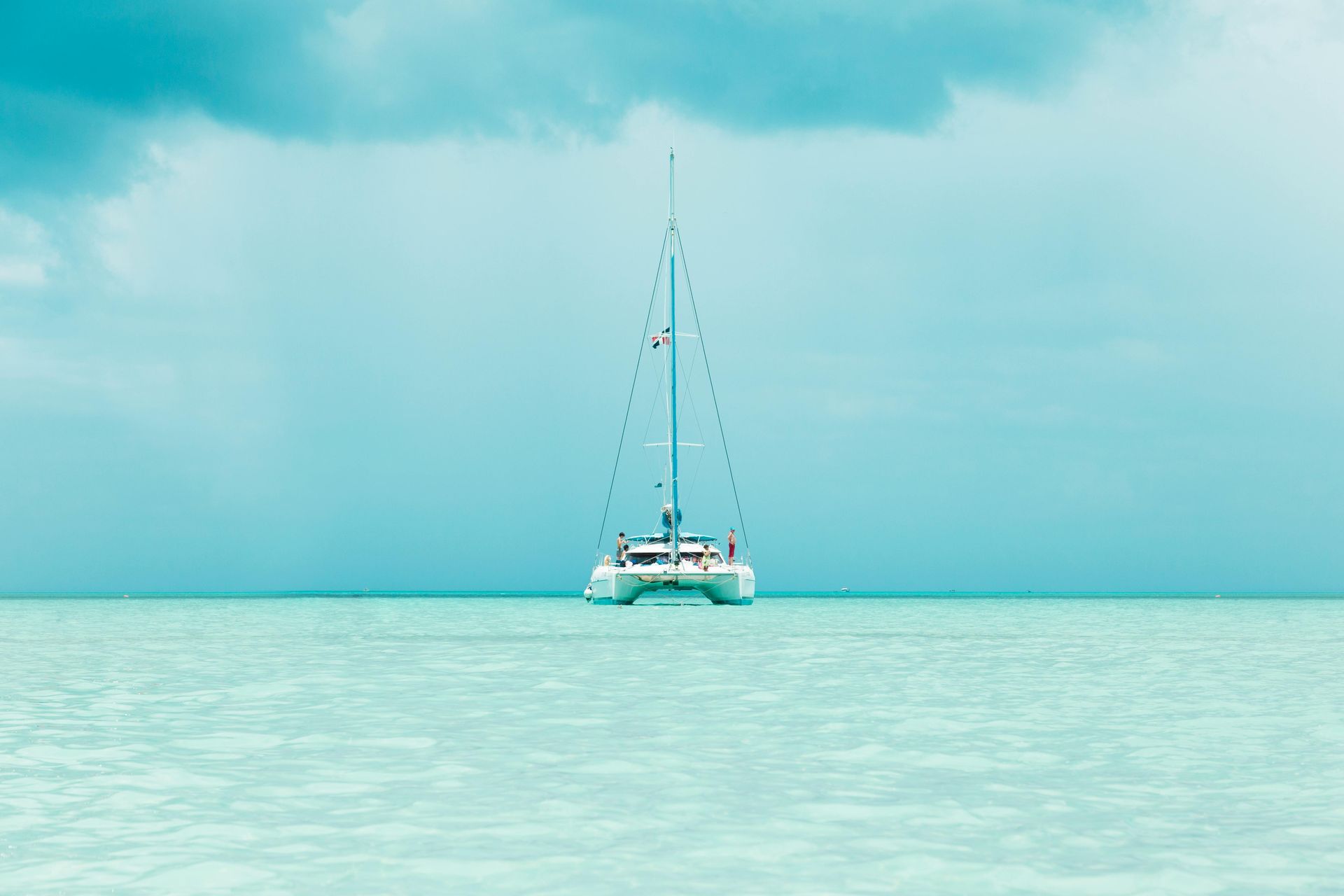 Catamaran sailing on turquoise water under a cloudy sky.