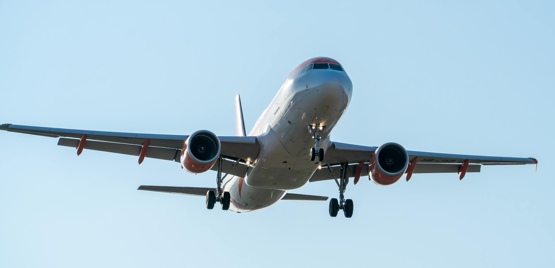 A passenger airplane with orange-accented engines approaches for landing against a clear, pale blue sky.