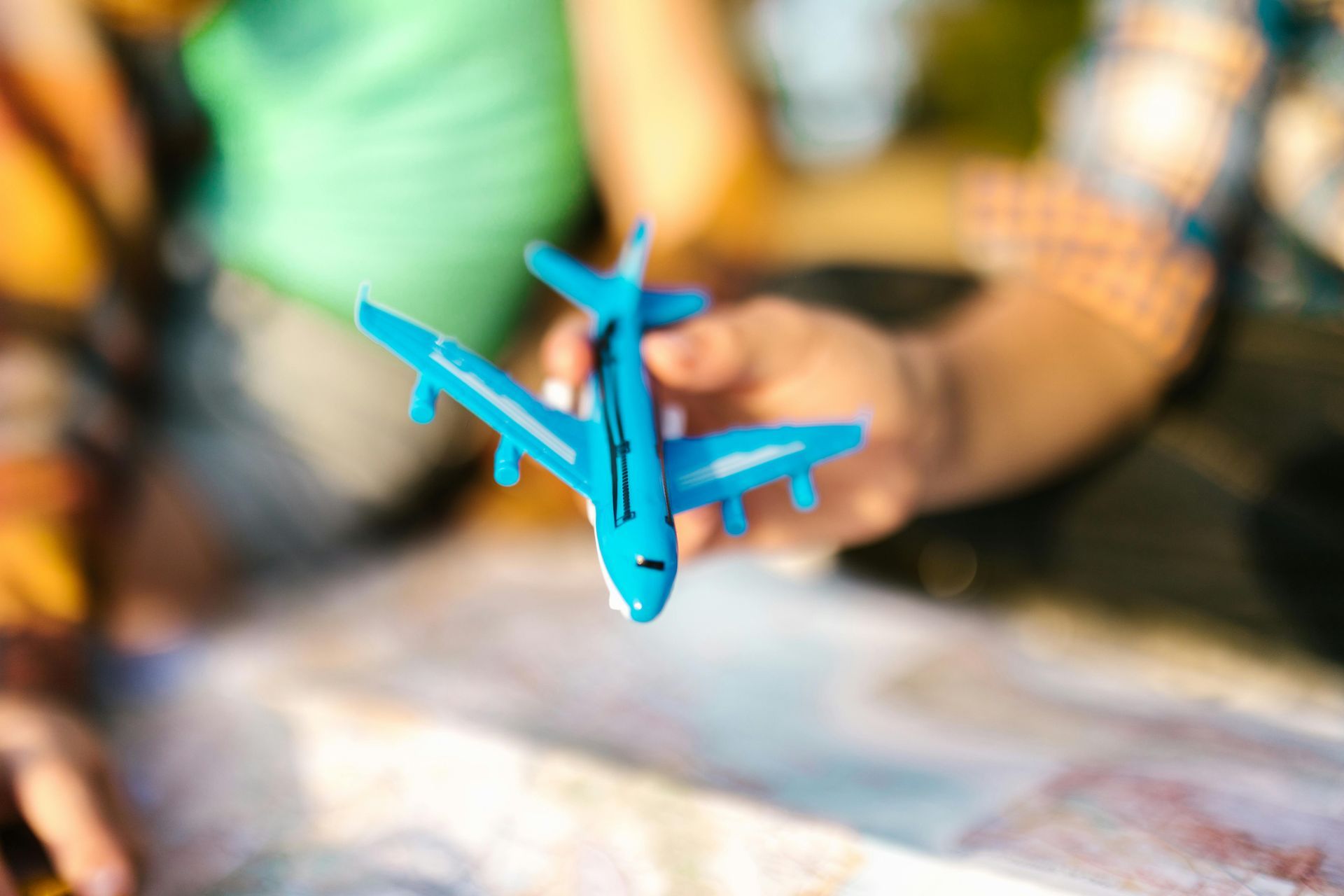 Hands holding a bright blue toy airplane over a blurred map background