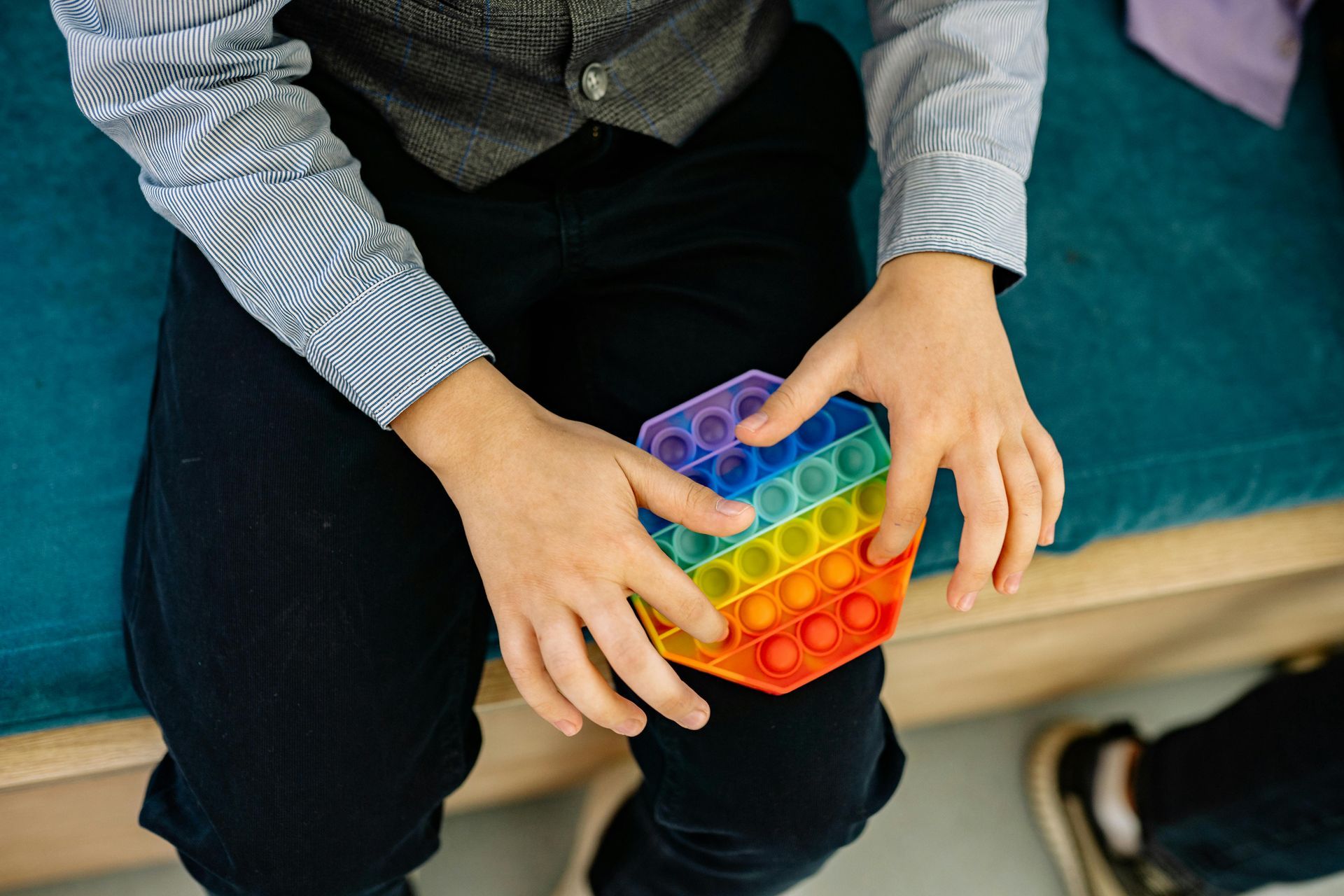 Hands holding a colorful rainbow silicone pop-it toy while sitting on a bench