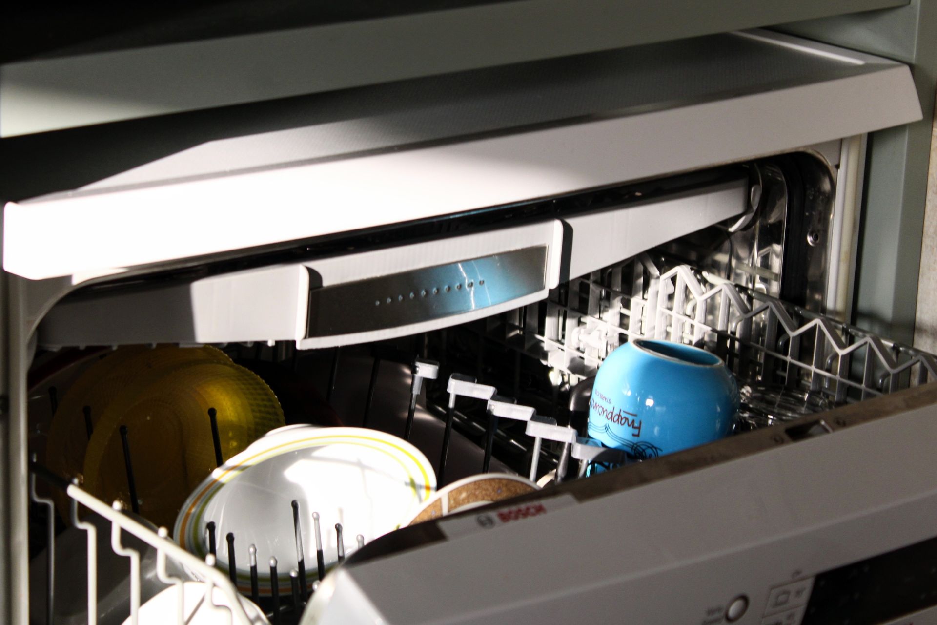 A bosch dishwasher is filled with dishes and cups