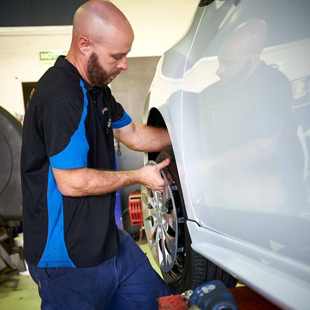 A Man in A Black and Blue Shirt Is Working on A Car — Smitty's Tyres & More In Taminda, NSW