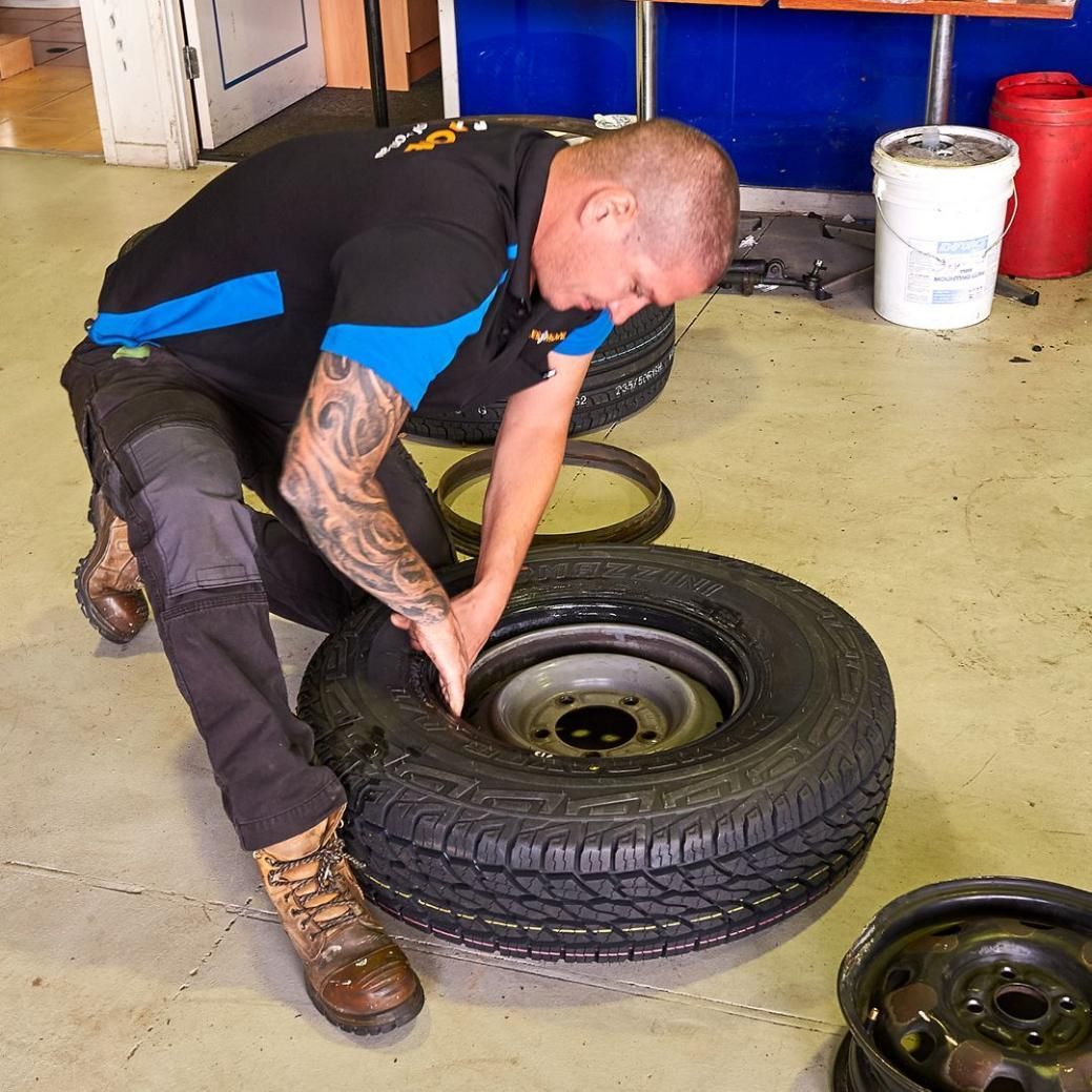 A Man with A Tattoo on His Arm Is Working on A Tire — Smitty's Tyres & More In Armidale, NSW
