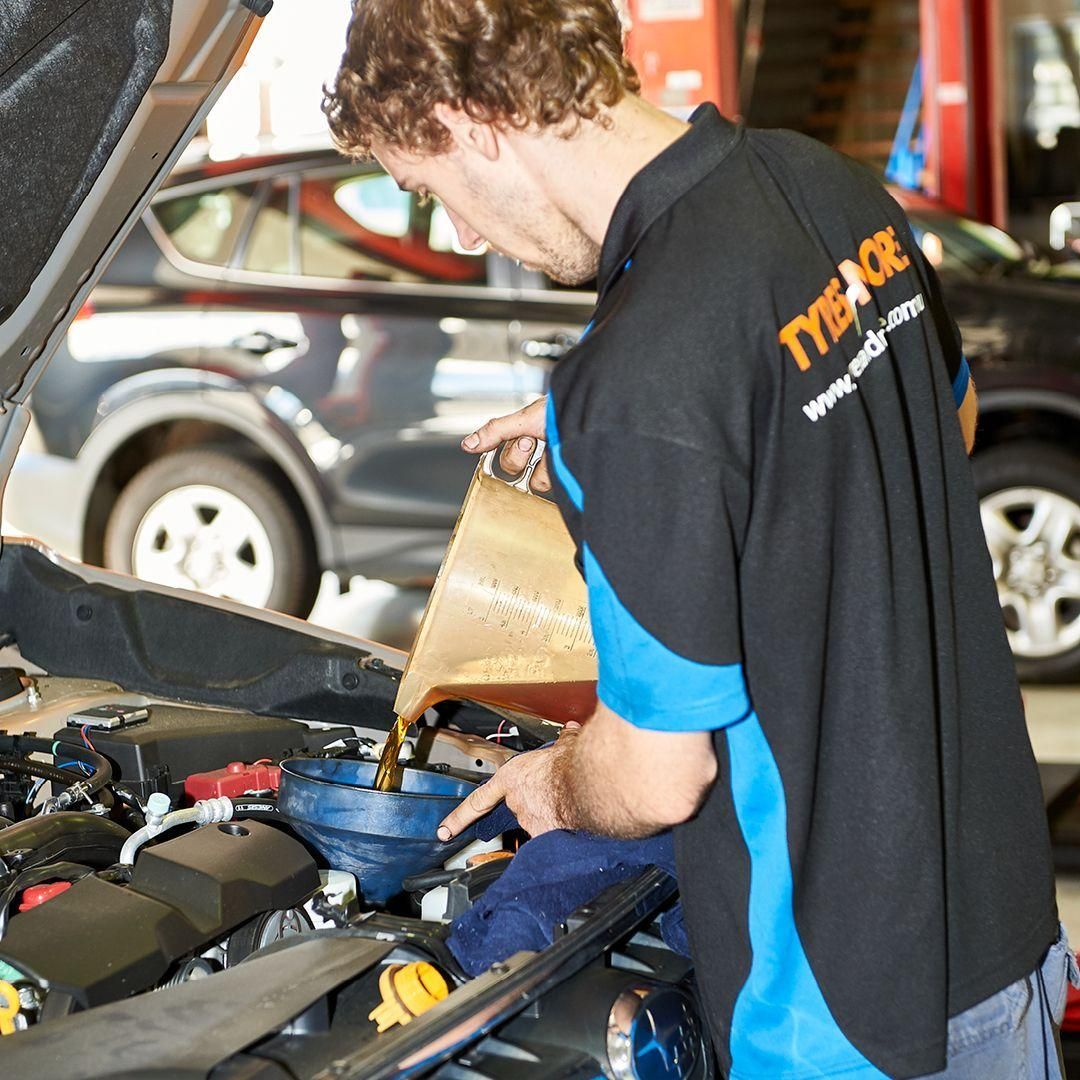 A Man Wearing a Black and Blue Shirt Is Pouring Oil Into a Car Engine — Smitty's Tyres & More In Quirindi, NSW