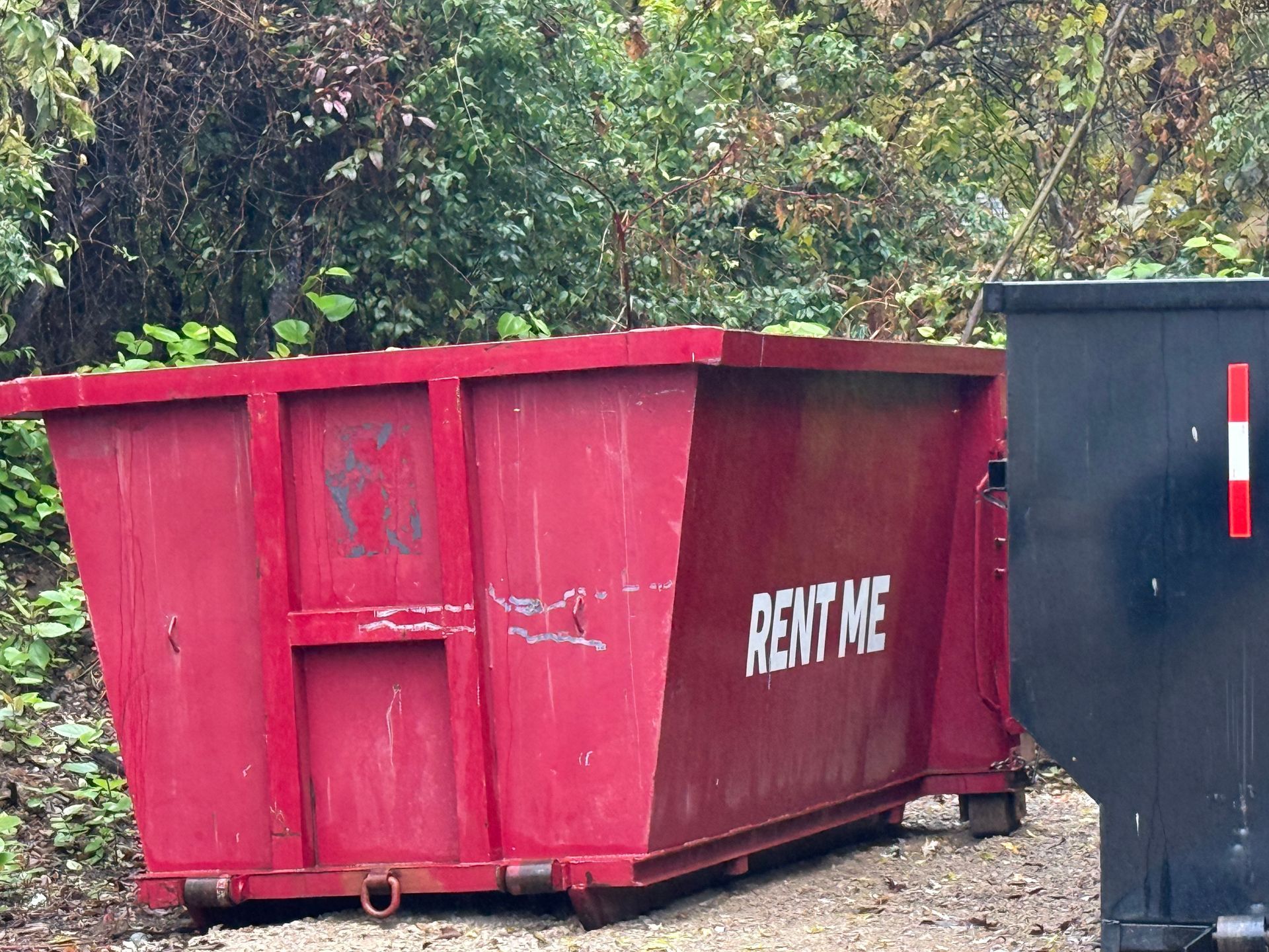 Blue dumpster filled with construction debris, in front of a partially built wooden house.