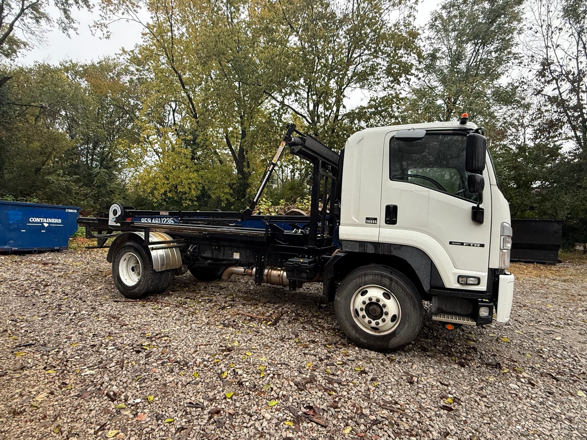 Yellow and red dumpster overflowing with debris on a sidewalk in front of buildings and trees.