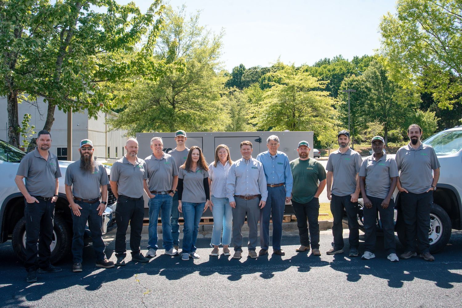 Group of people standing together outdoors in front of large trucks on a sunny day