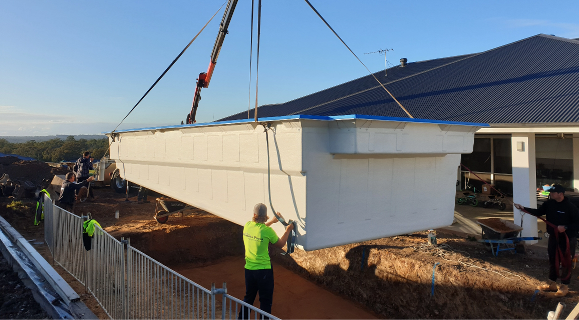 A crane is lifting a swimming pool into the ground.