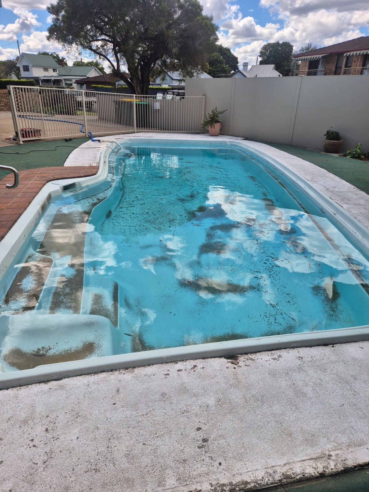 Dilapidated swimming pool with cracked and stained surface, visible steps, and a partially filled with water.