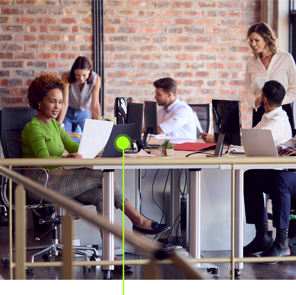 Um grupo de pessoas está sentado em mesas com computadores e laptops.