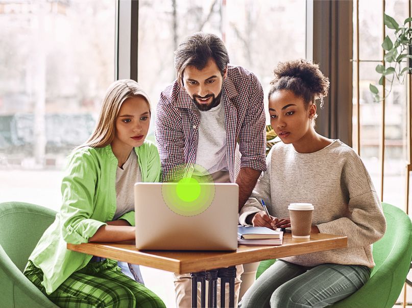 Um grupo de pessoas está sentado em uma mesa olhando para um laptop.