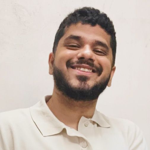 Um homem com barba está sorrindo e vestindo uma camisa pólo branca.