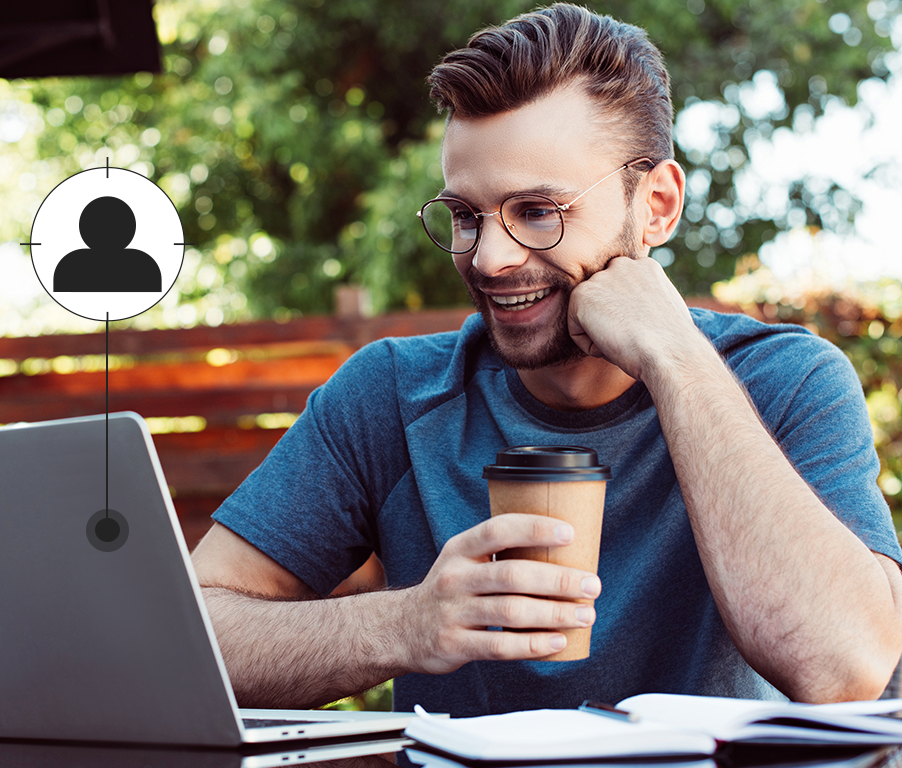 Um homem está sentado a uma mesa com um laptop e uma xícara de café.