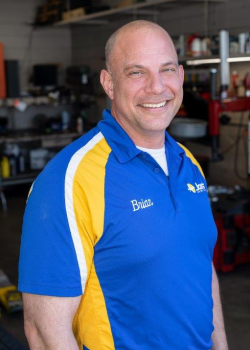 Man in blue and yellow uniform smiles in auto shop.