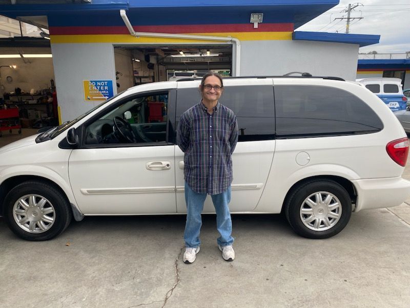 Man standing in front of a white minivan at a car repair shop.
