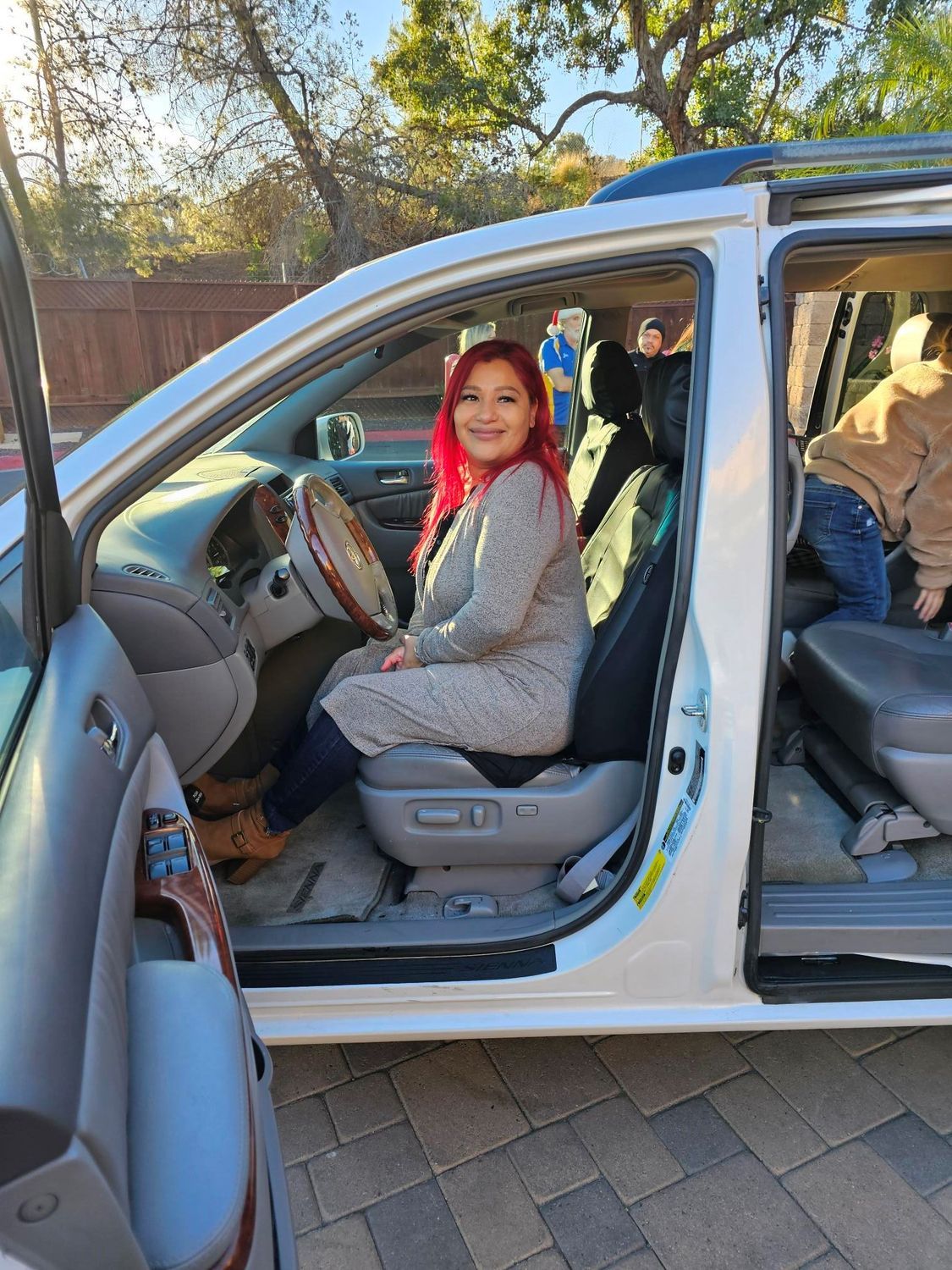 Woman with red hair sits in a white minivan, smiling. A child climbs into the back.