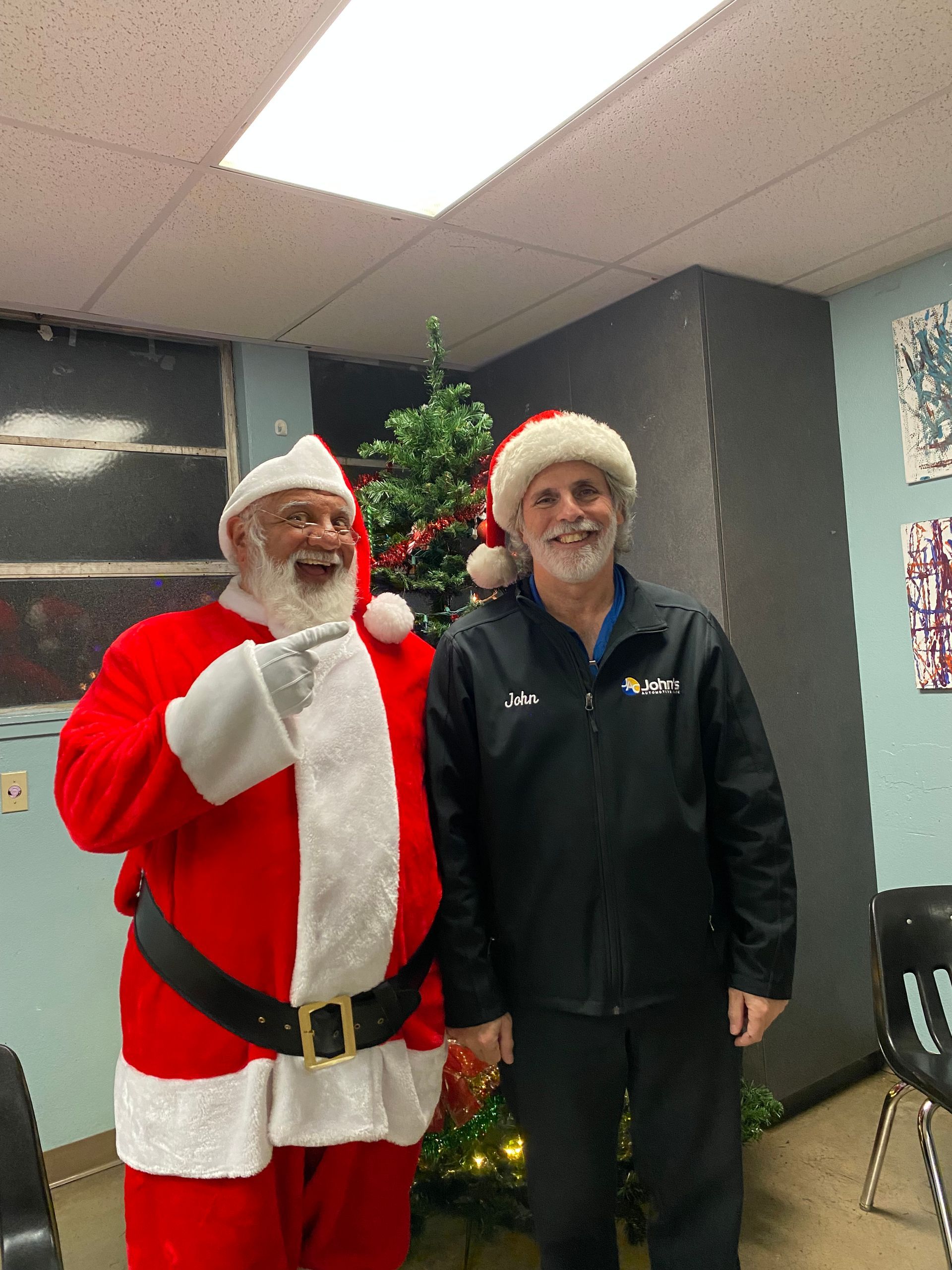 Santa Claus and a man in a black jacket smiling, posing by a Christmas tree.