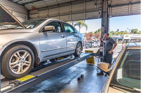 Silver car raised on a lift in a garage, mechanic standing by.