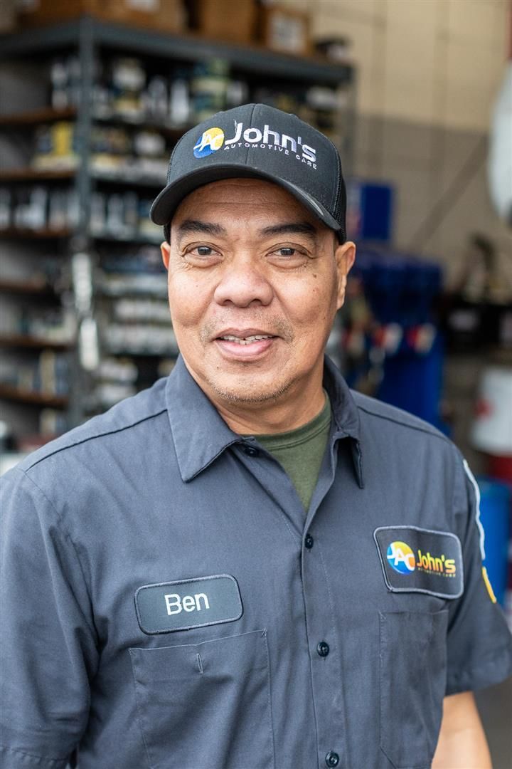 Man in mechanic uniform and hat smiling, in a shop.