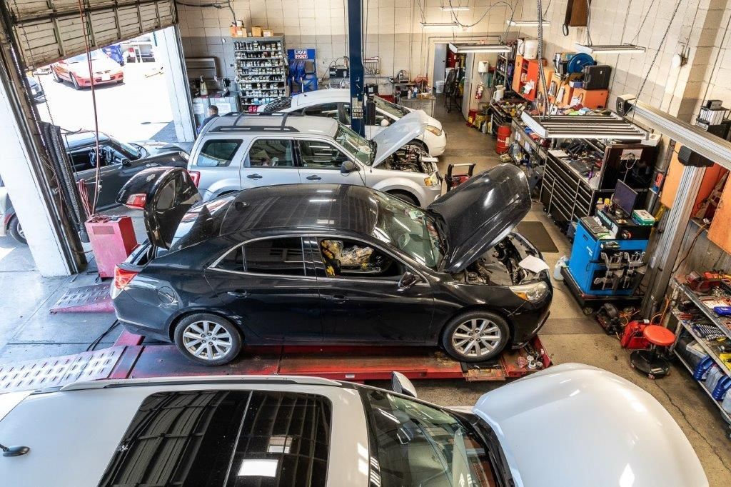 Cars in various states of repair inside a busy auto repair shop with tools and equipment visible.