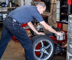 Mechanic in a shop working on a car tire, using a tool.