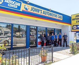 John's Automotive Care shop exterior with staff standing in front. Blue and yellow signage.