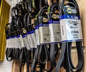 Rows of black automotive belts with NAPA labels hanging on a wooden wall.