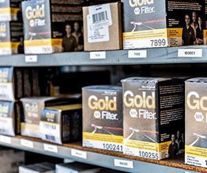 Shelves stocked with Gold Q Filter boxes in a warehouse setting, showing various product labels and codes.