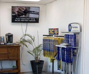Auto shop interior with wiper blade display, TV screen, potted plant, and coffee maker.