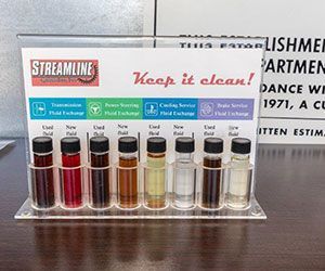 A display showing samples of used and new fluids. The fluids are labeled for transmission, power steering, and cooling services.