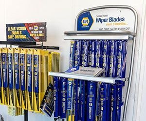 NAPA wiper blades displayed on a metal rack. Blue and yellow packaging. Store setting.