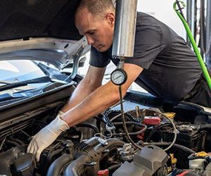Mechanic in a shop works on a car engine, checking it with a gauge.