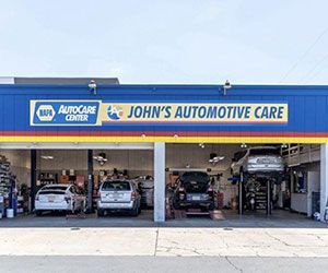John's Automotive Care shop with vehicles on lifts, under a blue and yellow awning.
