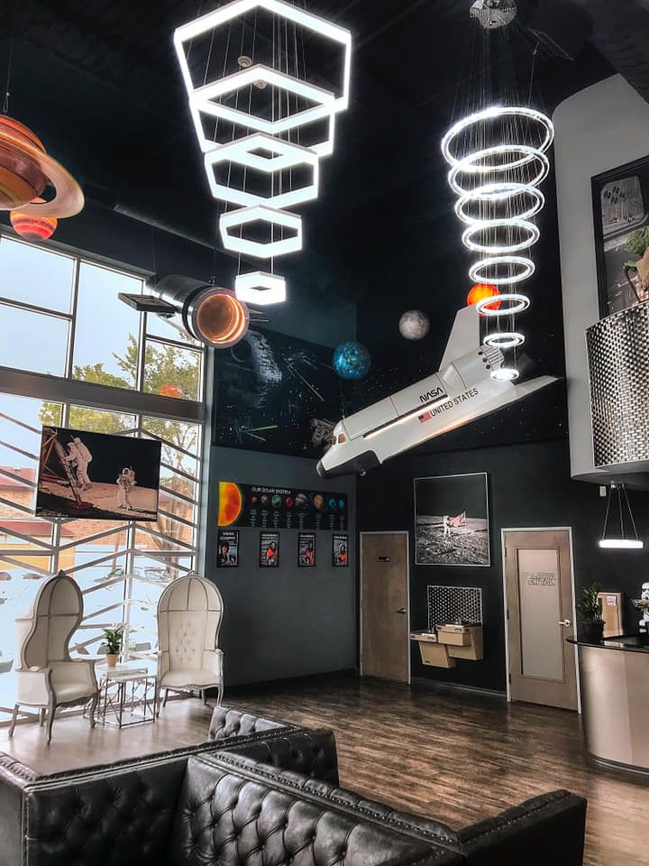 Space-themed interior: lounge with planets, a shuttle, and geometric lights. Shows a sofa and chairs.