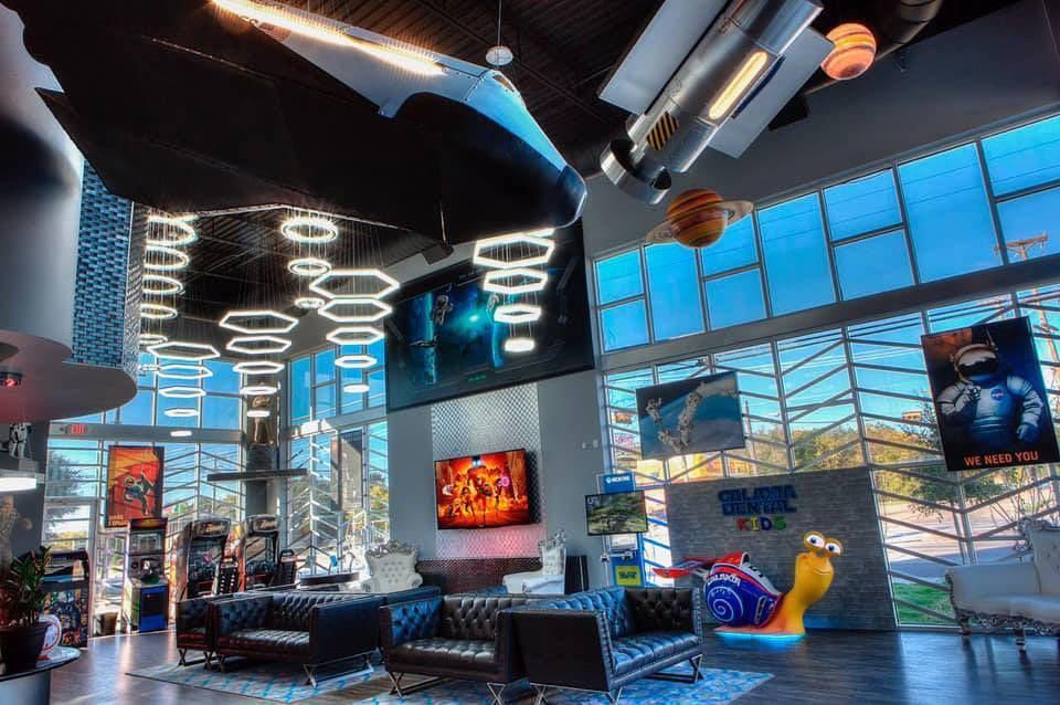 Interior of a space-themed arcade with seating, games, and a large video screen.