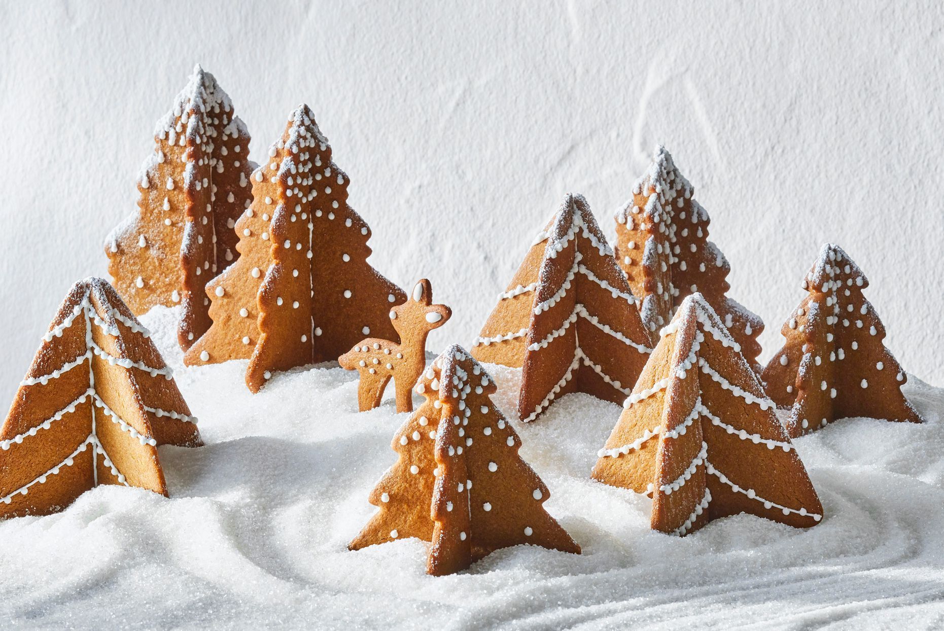 This photo shows some cookies made of ginger bread shaped like trees with a snowy background.