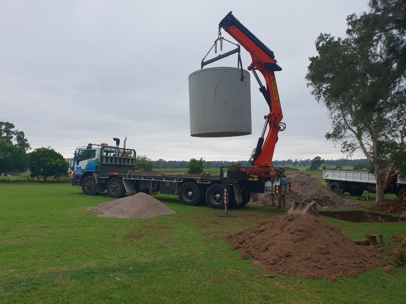 a crane is lifting a large concrete cylinder from a truck .