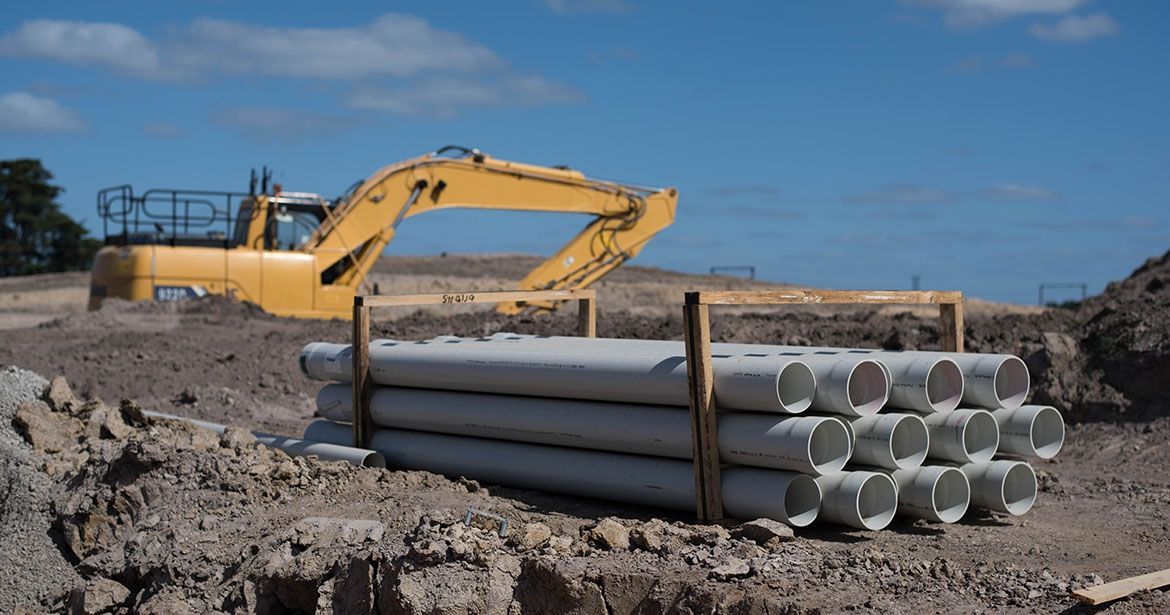 a construction site with a yellow excavator and a pile of pipes .